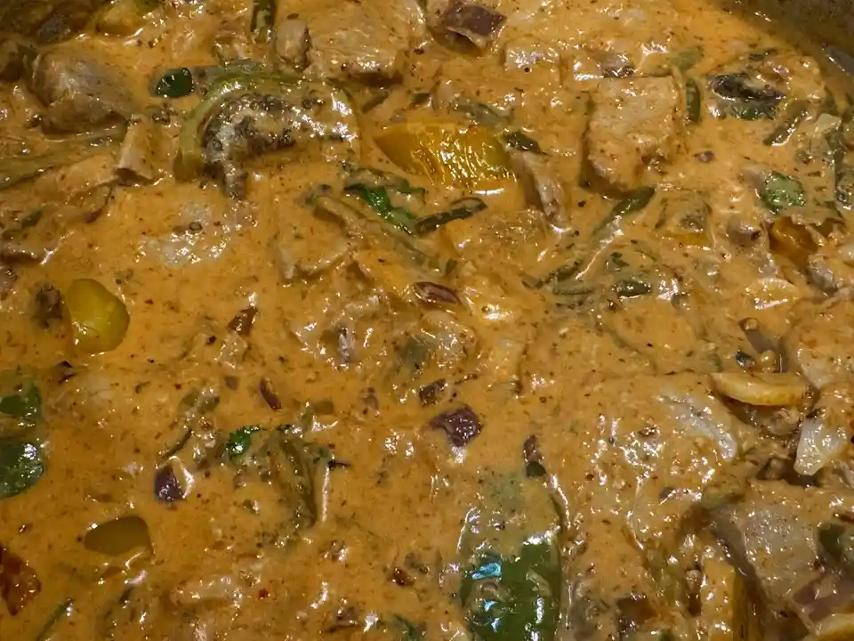 A close-up photo of a thick, orange-brown curry sauce with chunks of meat, green peppers, onions, and spices. The overlaid…