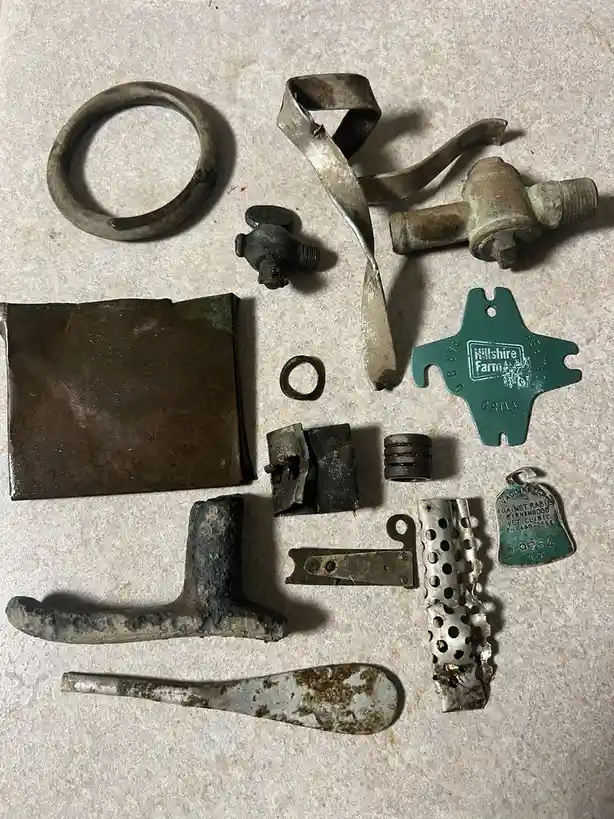 An overhead shot displays a scattered collection of corroded, rusty, and weathered metal objects on a light-colored surface…