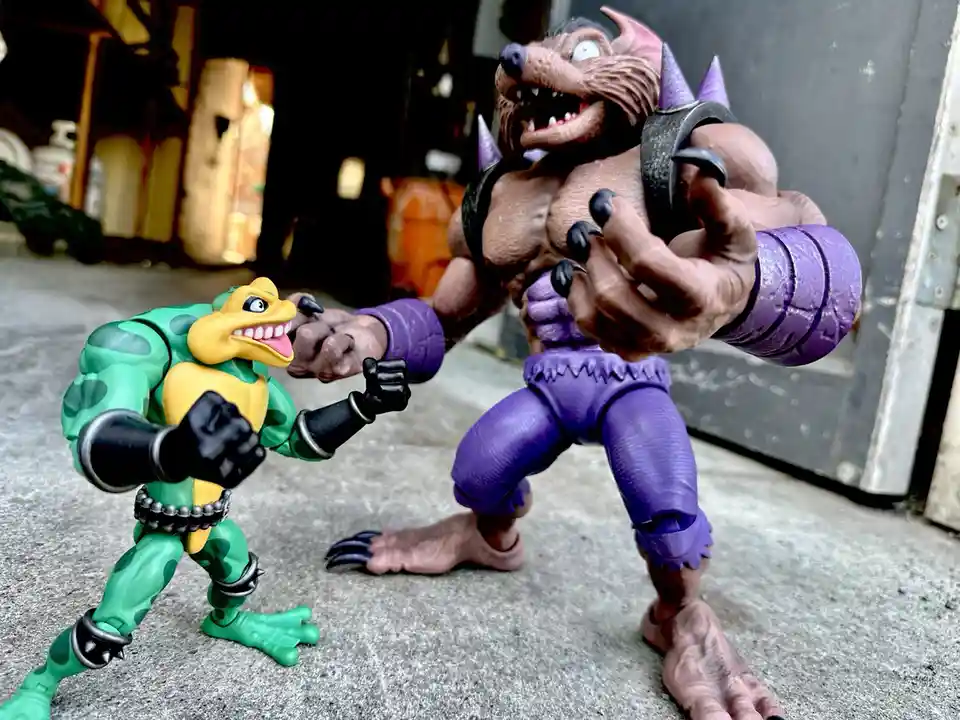 Two action figures are posed in a confrontational stance on a concrete floor. The smaller figure on the left is green and…