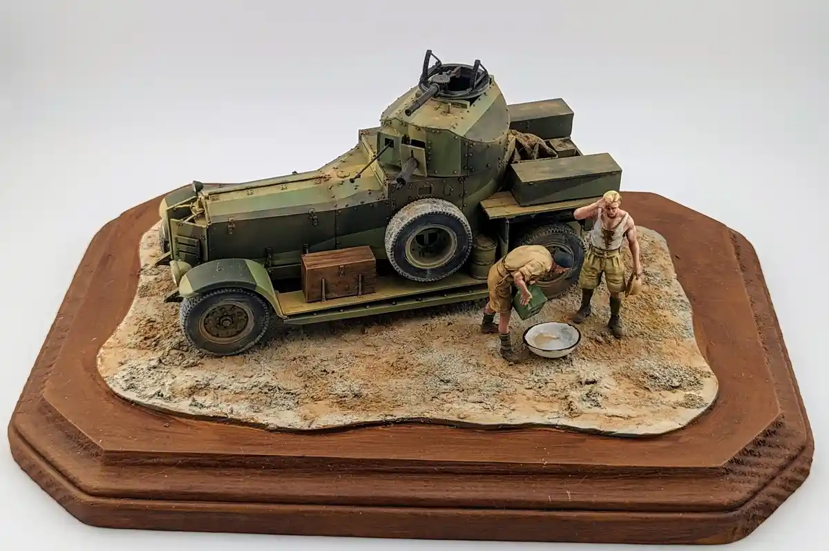 A detailed diorama of a military armored car on a wooden base, with two miniature soldiers—one pouring liquid from a green…