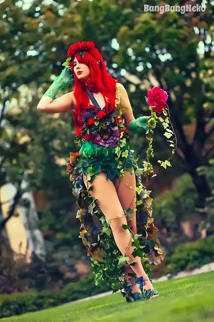 A person with long red hair is cosplaying as Poison Ivy, wearing a costume made of green leaves and red flowers, holding a…