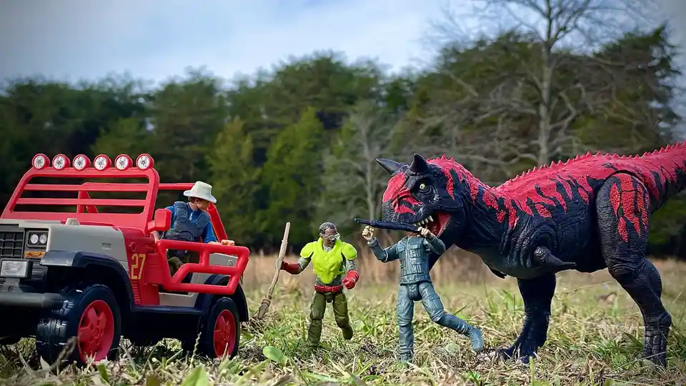 A staged outdoor scene features toy action figures and a toy dinosaur in a grassy field. One figure is in a red and gray toy…