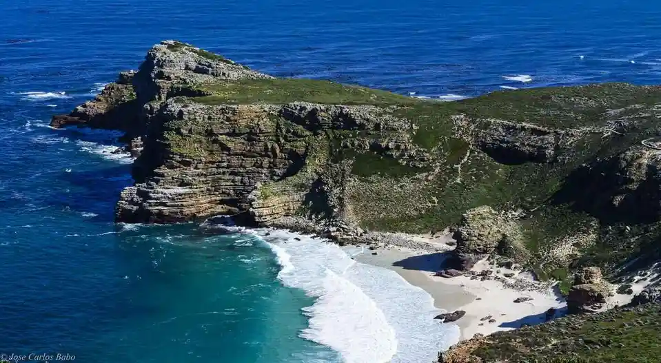 a stunning aerial photograph of a secluded beach nestled between dramatic, layered cliffs overlooking deep blue ocean waters…