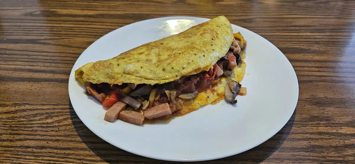 A close-up photo shows a folded, golden-yellow omelette on a white plate, revealing a filling of chopped mushrooms, red…