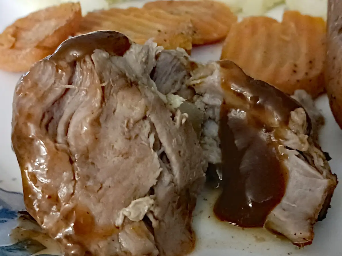 A close-up photo shows a piece of cooked meat, likely pork, covered in brown gravy and served with crinkle-cut fries on a…