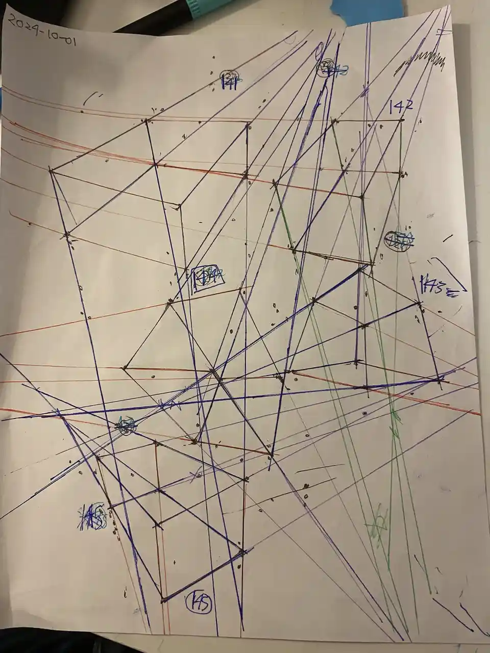 A white sheet of paper covered in a chaotic, overlapping web of hand-drawn lines in blue, orange, and green markers. Several…