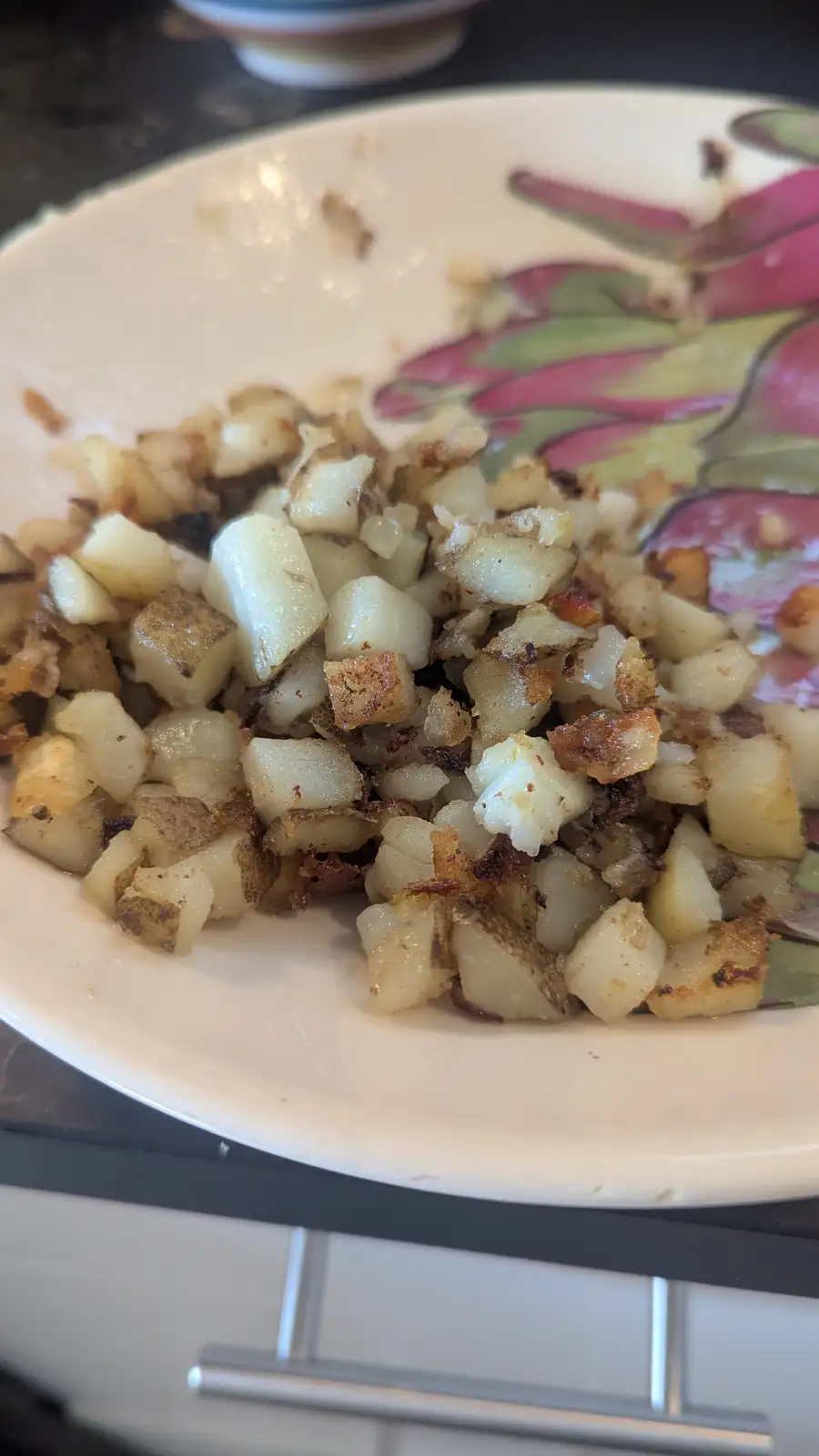 A close-up photo shows a plate of crispy, golden-brown home-fried diced potatoes on a white plate with a pink and green…