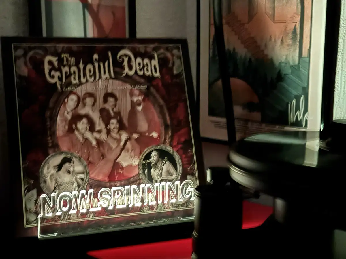 A framed poster of The Grateful Dead album cover is displayed next to a record player, with the text 'NOW SPINNING' overlaid…
