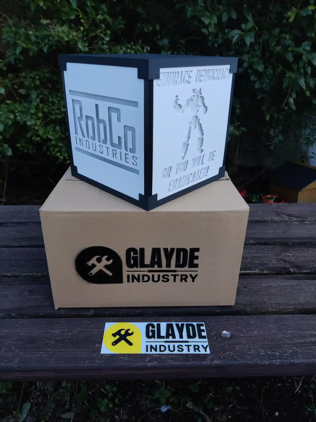 A white cube with black trim sits atop a brown cardboard box, both branded with 'GLAYDE INDUSTRY' logos. The cube's visible…