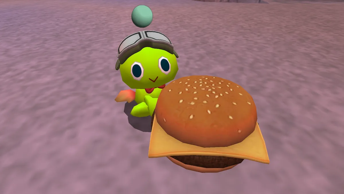 A green, cartoonish turtle-like character wearing aviator goggles and a red bowtie stands beside a giant sesame seed…
