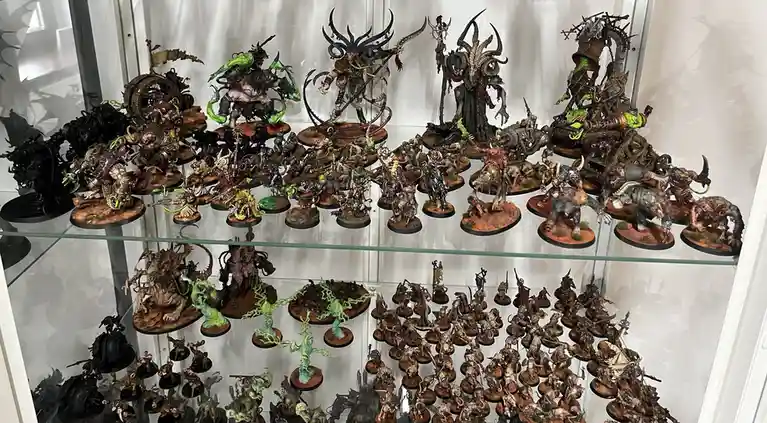 A glass display case filled with hundreds of intricately painted fantasy miniatures, mostly depicting grotesque, monstrous…