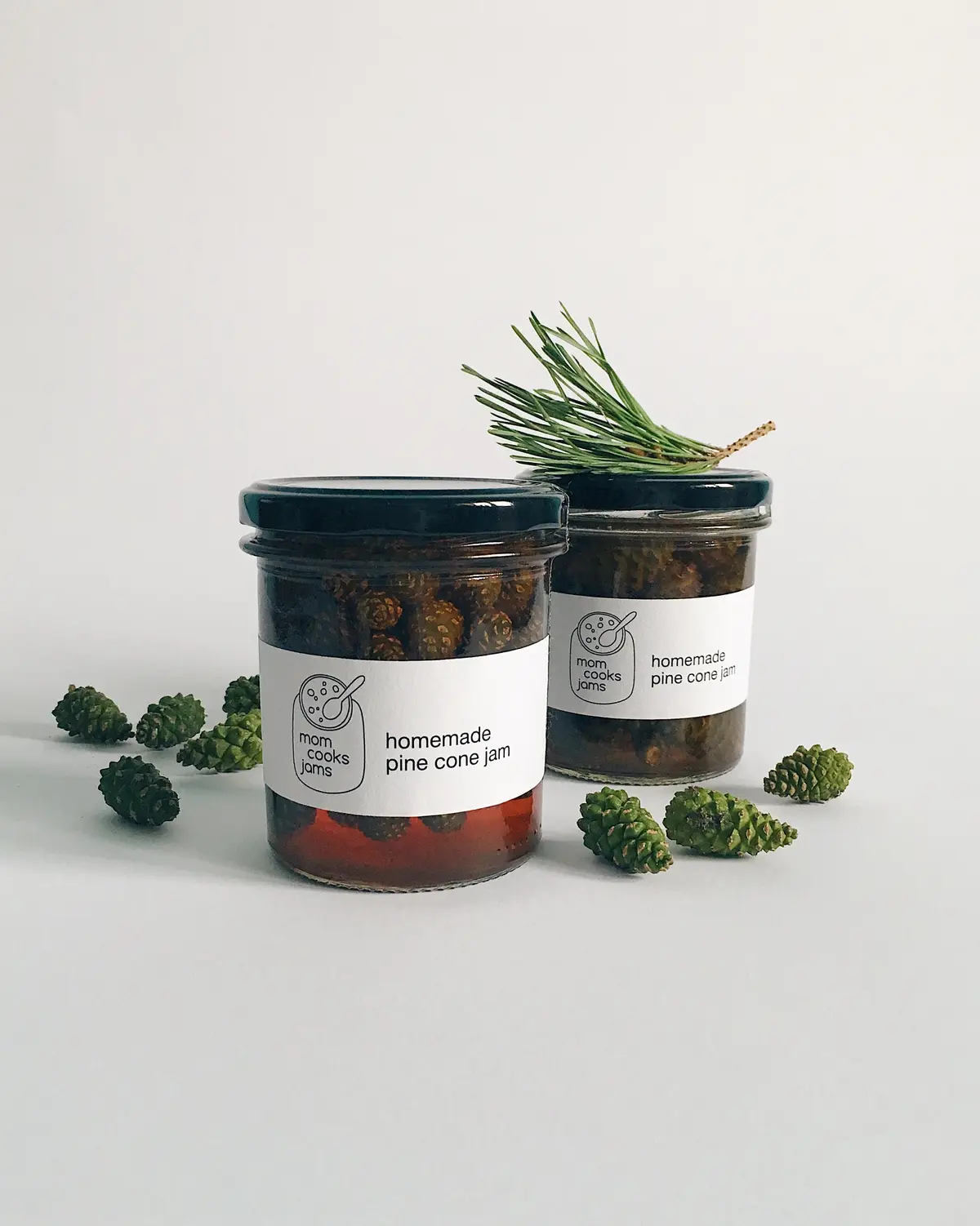 Two glass jars filled with what appears to be pine cone jam, each labeled 'homemade pine cone jam' with a 'mom cooks jams'…