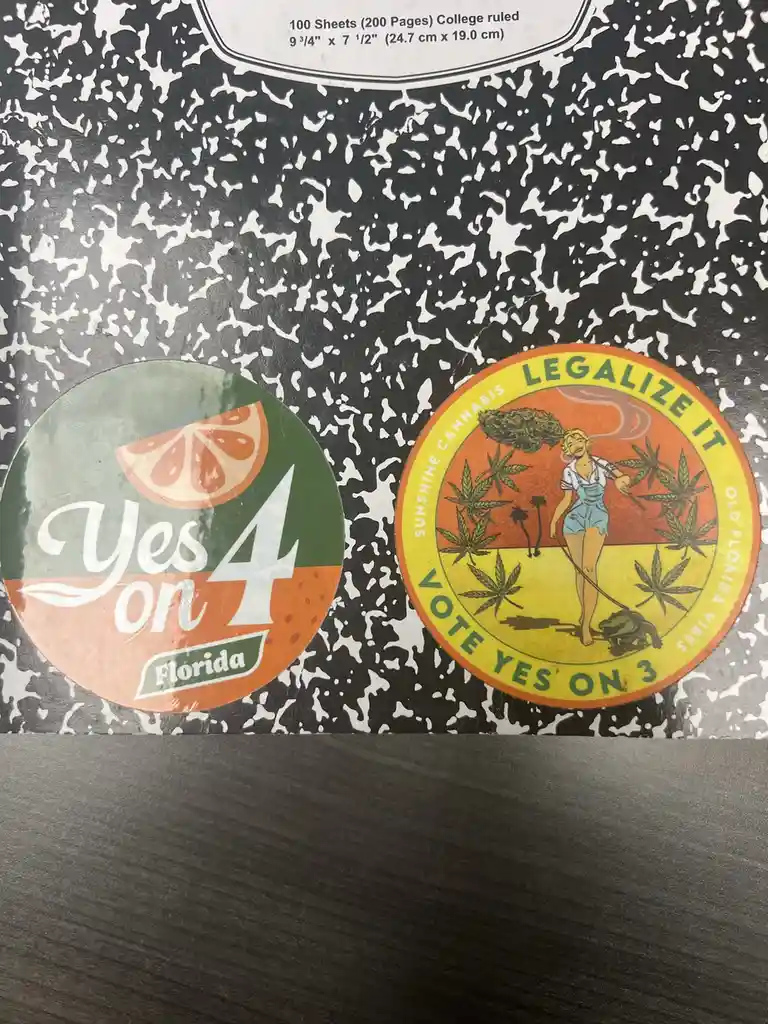 Two circular political stickers are placed on a black-and-white speckled notebook. The left sticker says 'Yes on 4 Florida'…