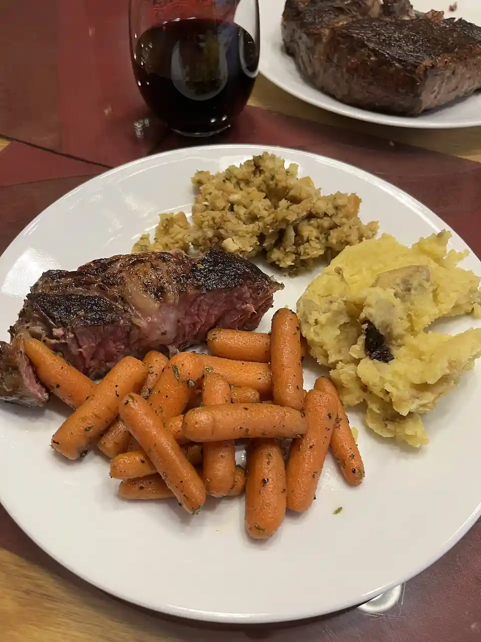A close-up photo of a plated meal featuring a sliced medium-rare steak, baby carrots, mashed potatoes with a dark inclusion…