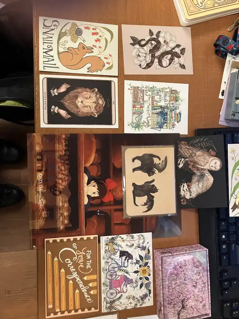 An overhead shot of a wooden desk covered with various decorative postcards and stationery items, including a 'Snail Mail'…