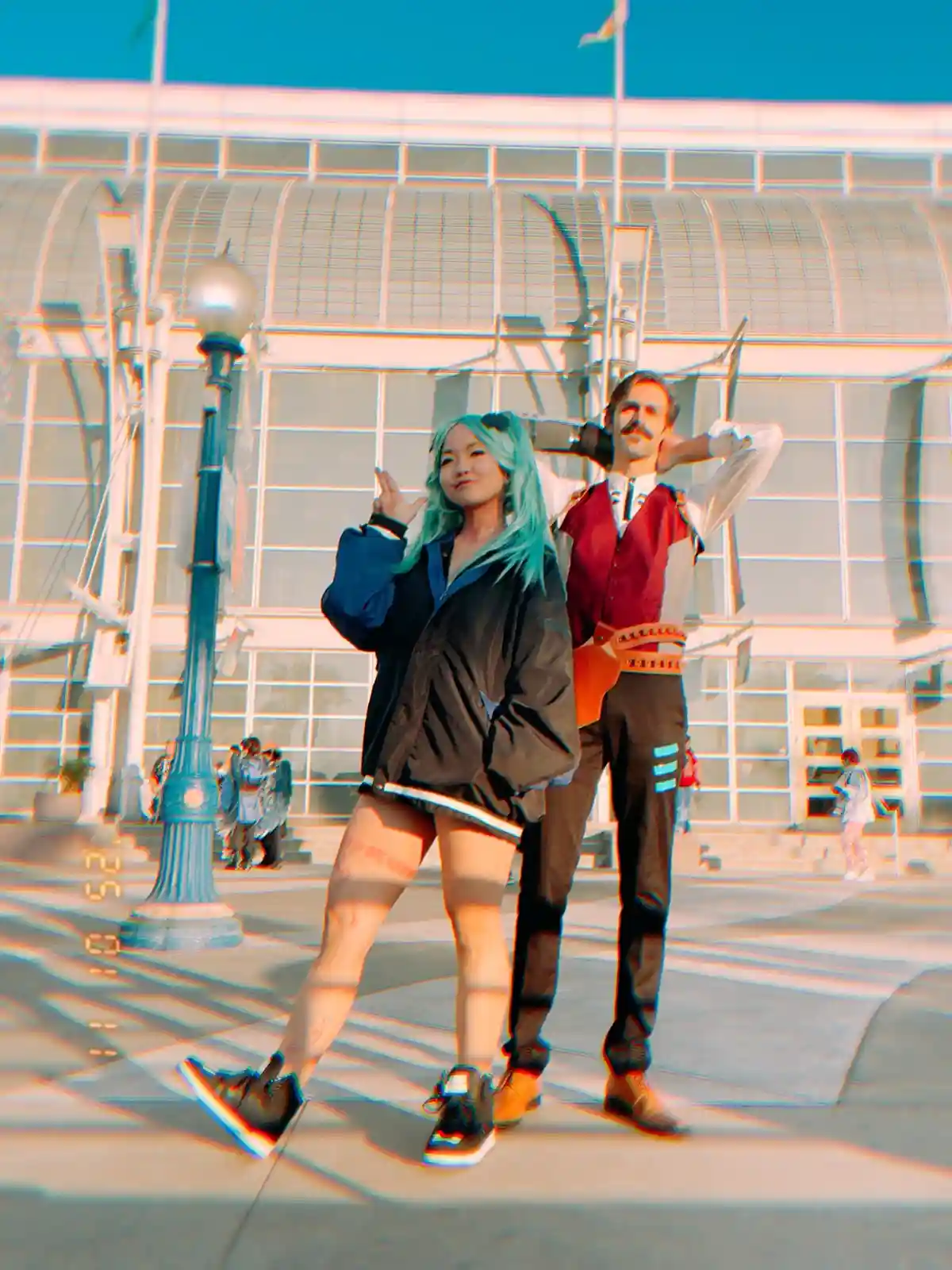 Two people in cosplay pose outdoors in front of a modern building with a strong anaglyph 3D effect applied, causing color…