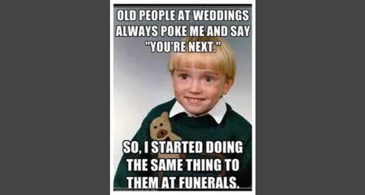 A young child with blonde hair and a green sweater holding a teddy bear looks at the camera with a slightly awkward, forced…