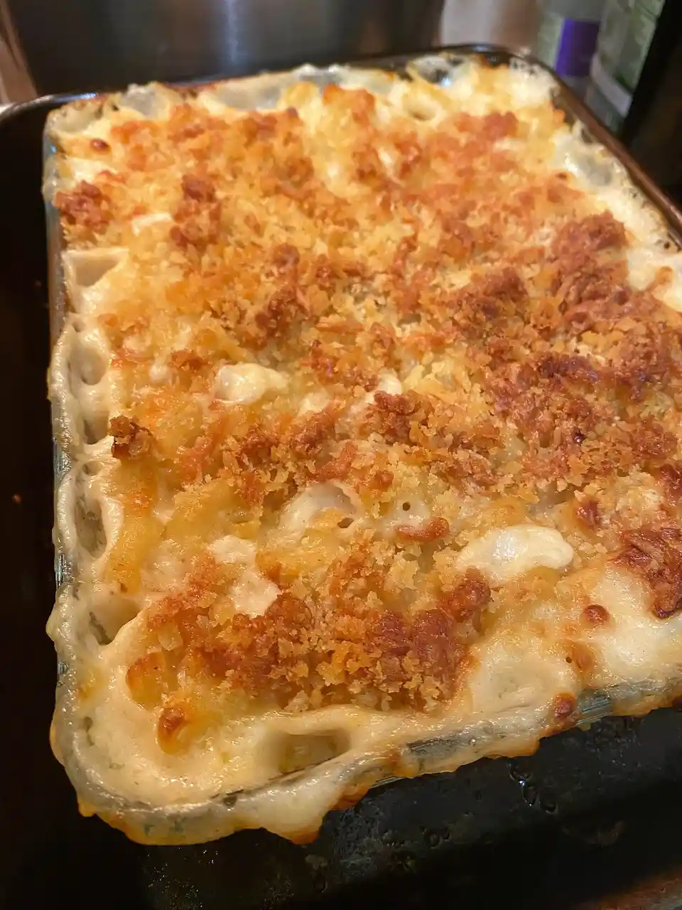 A close-up photo of a freshly baked macaroni and cheese casserole in a glass baking dish, featuring a golden-brown, crispy…