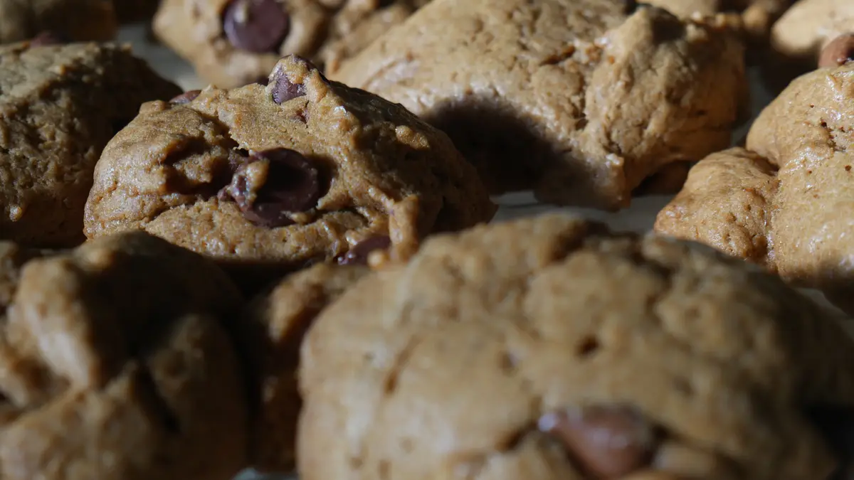 A close-up photo of several golden-brown chocolate chip cookies with visible chocolate chips, arranged closely together. The…