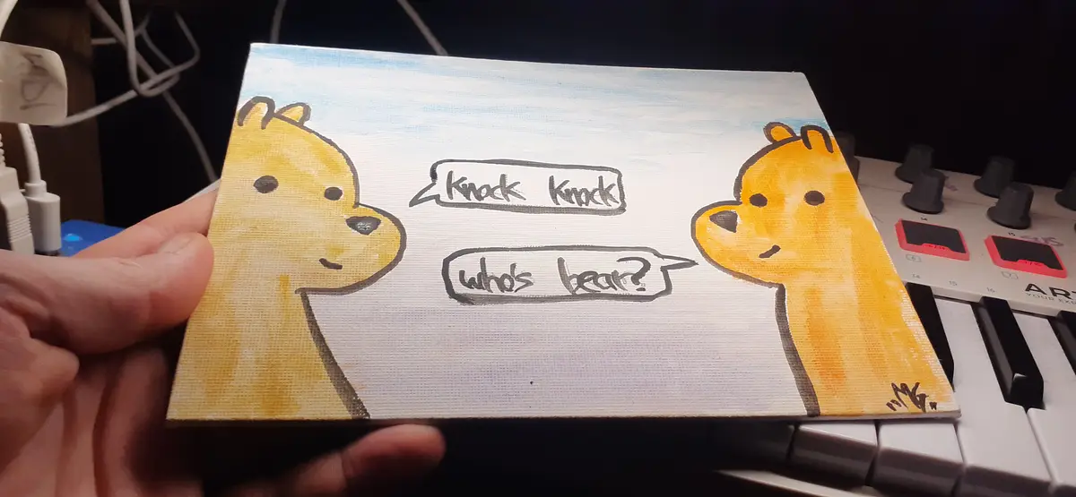A hand holds a small painted canvas featuring two cartoon bears facing each other. The bear on the left has a speech bubble…