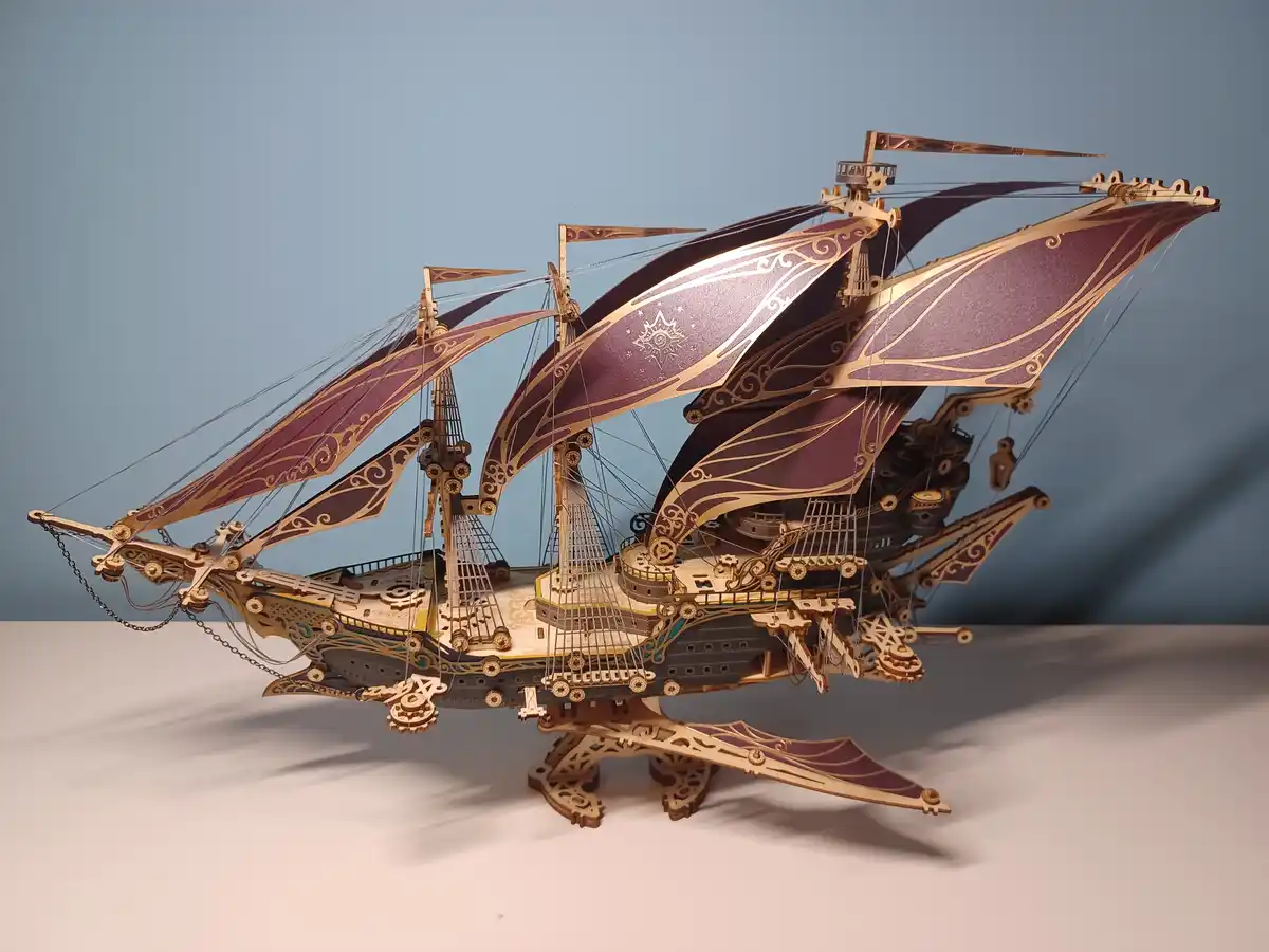 A highly detailed, ornate wooden model of a fantasy sailing ship with purple and gold sails, intricate carvings, and visible…