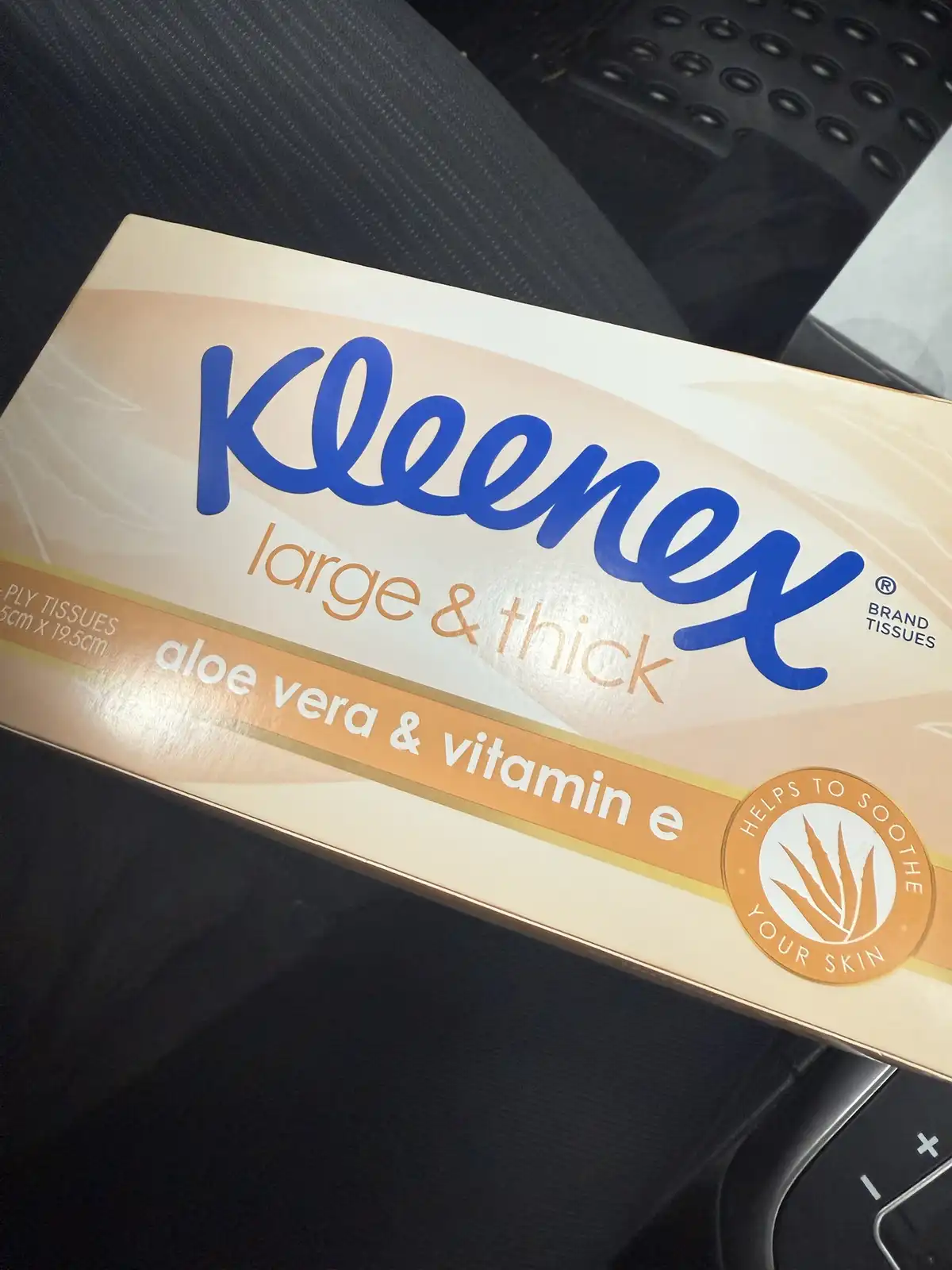 A close-up photo shows a box of Kleenex brand tissues resting on a car seat, with visible text reading 'large & thick'…