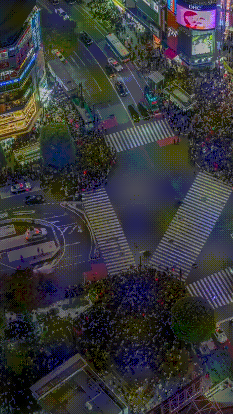 A time-lapse aerial view of a busy city intersection at night, showing a white car driving through a dense crowd of…