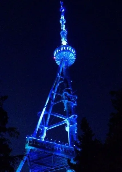 A tall, metal lattice tower with a spherical observation deck near the top is illuminated in bright blue light against a…