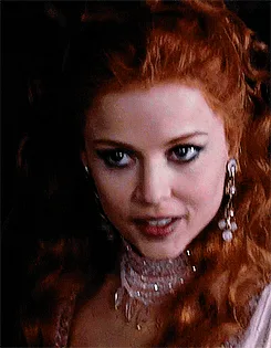 Six identical stills of a woman with red hair, heavy eyeliner, and ornate jewelry show her expression subtly shifting from…