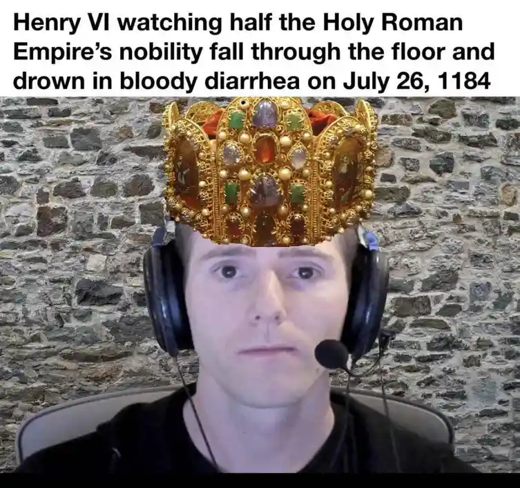 A man wearing a headset and a black shirt sits in front of a stone wall, with a large, ornate golden crown with jewels…