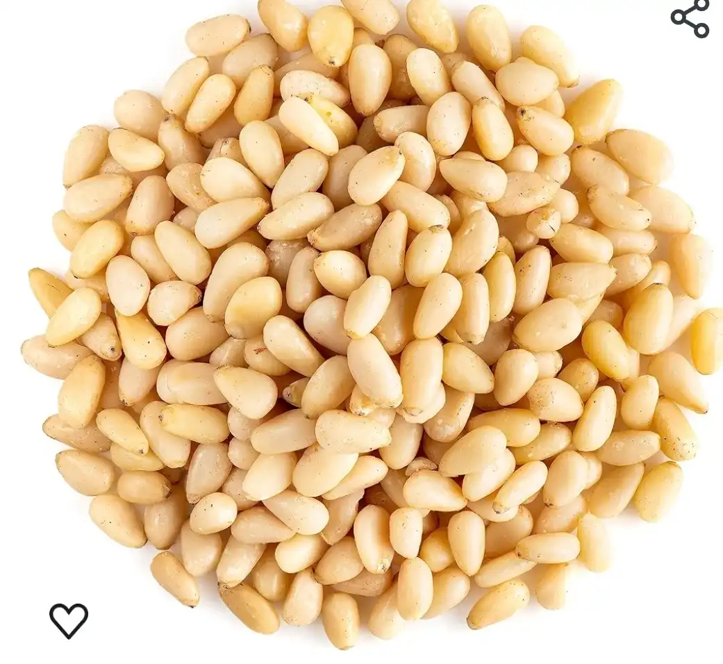 A top-down photo shows a pile of light beige pine nuts on a white background. In the bottom left corner, there is a black…