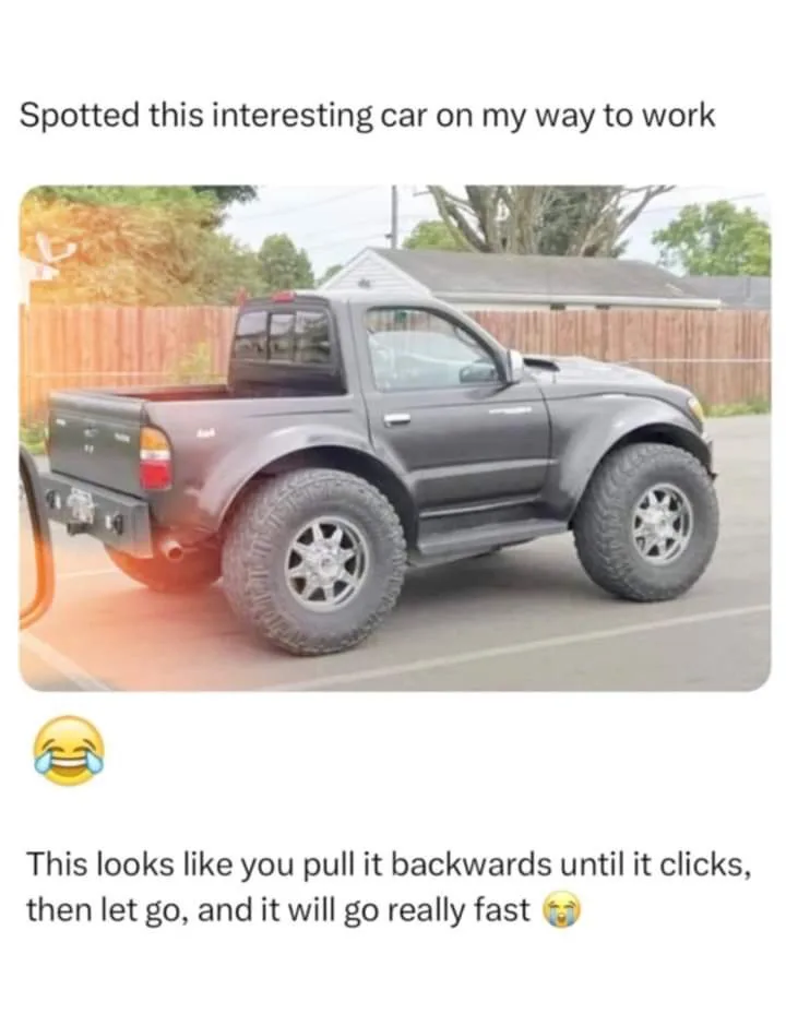 A dark gray pickup truck with oversized, knobby tires and a lifted suspension is parked in a lot. The overlaid text reads…