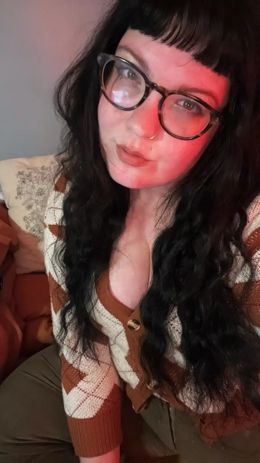 A person with long dark hair, bangs, and tortoiseshell glasses looks directly at the camera with a slightly tilted head and…