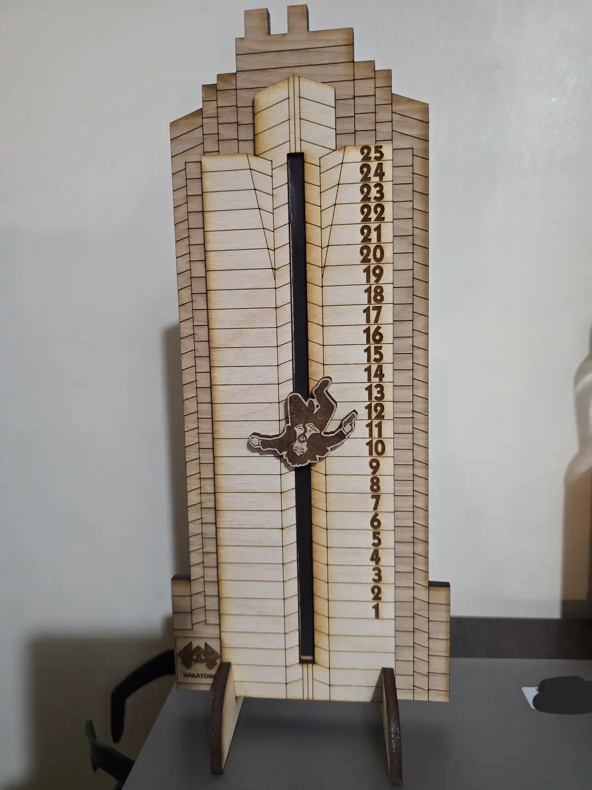 A wooden model of the Nakatomi Plaza building from the movie Die Hard, featuring a vertical scale with floor numbers 1 to 25…