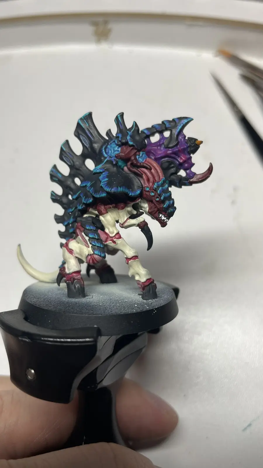 A close-up photo shows a highly detailed, painted fantasy miniature of a monstrous creature with a spiky black and blue…