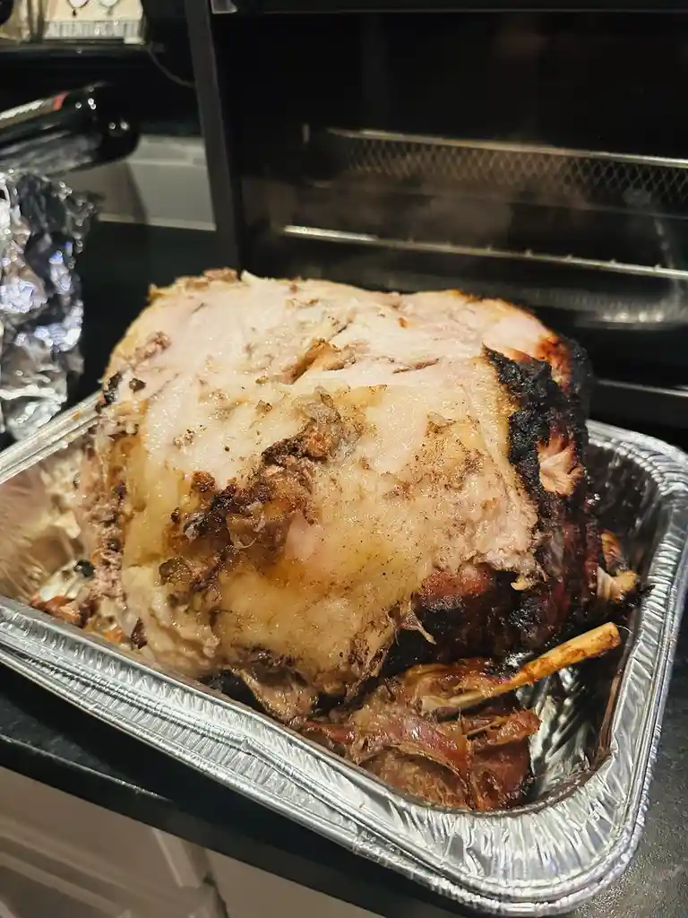 A roasted turkey sits in a foil pan, partially cooked with uneven browning and charred edges, placed in front of an open…