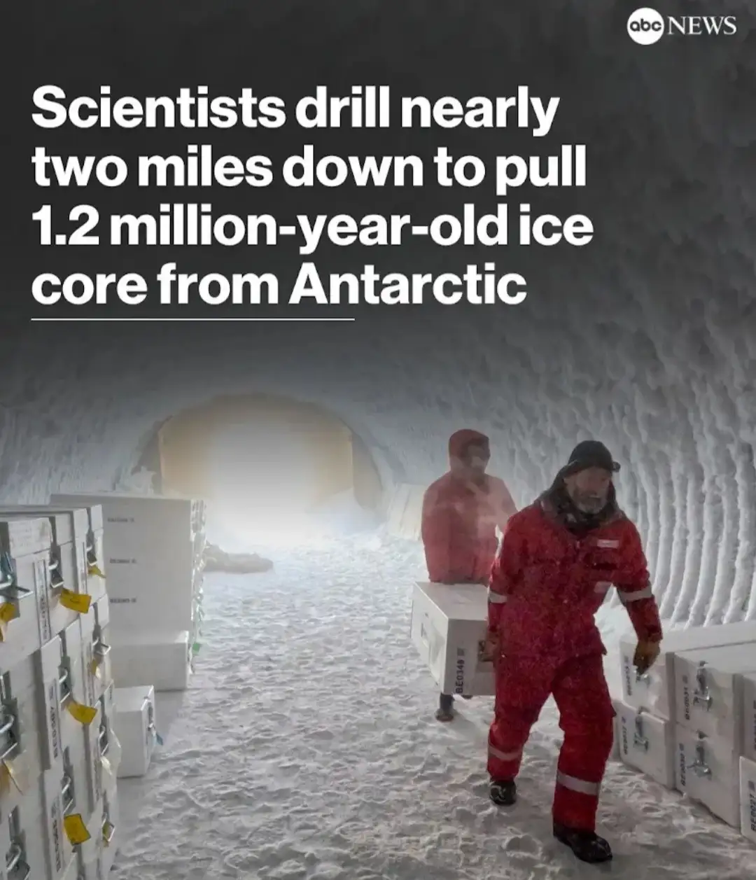 Two scientists in red insulated suits walk through a snowy tunnel, carrying large white boxes labeled with codes like…