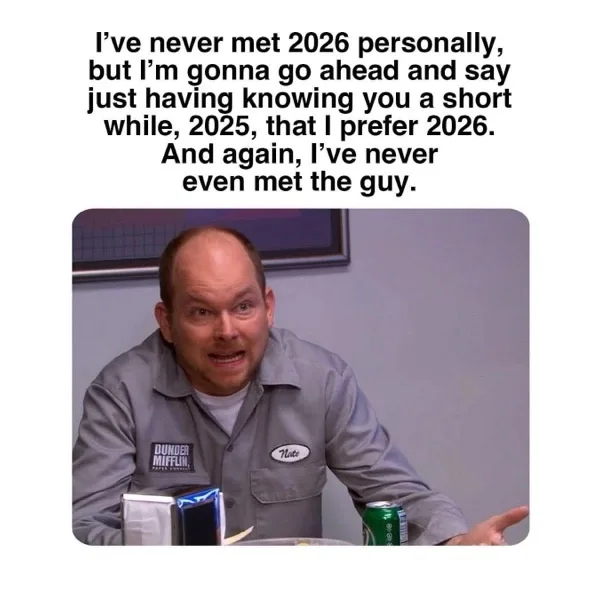 A man in a gray work shirt with a name tag reading 'Nate' and a 'Dunder Mifflin' logo sits at a table with a green soda can…