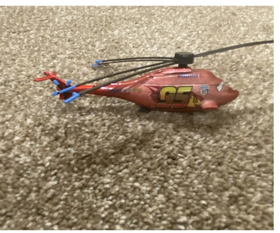 A red toy helicopter with Lightning McQueen's number 95 and sponsor logos from the movie Cars is lying on its side on a…