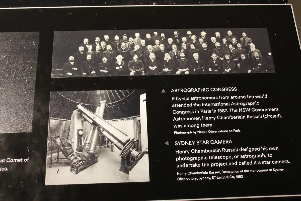 A museum exhibit panel displays two black-and-white photos: one of a large group of 19th-century astronomers with one man…