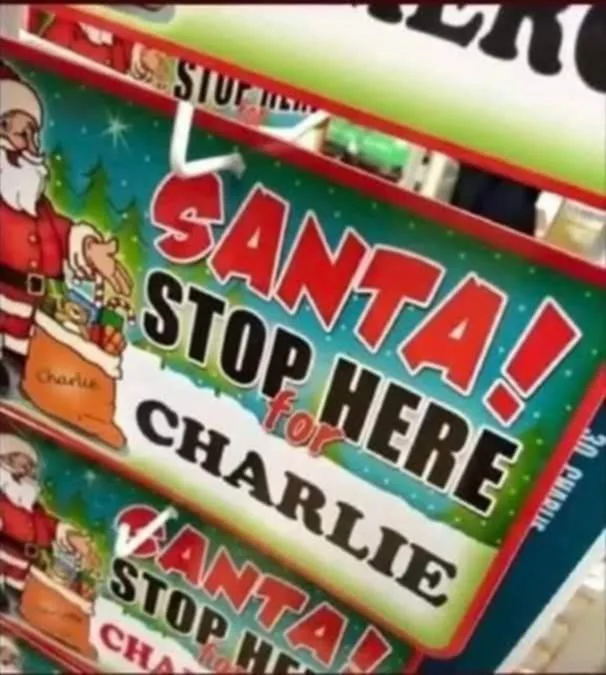 A close-up of a festive, colorful sign featuring an illustration of Santa Claus holding a sack labeled 'Charlie'. The sign…