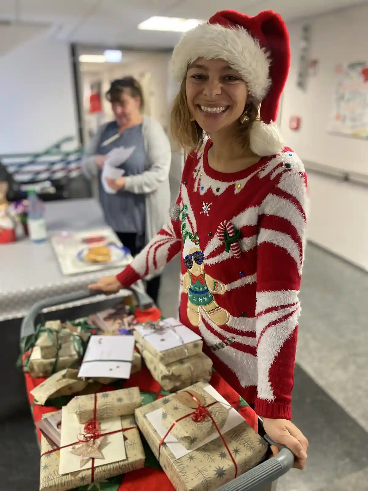 A woman wearing a red and white Santa hat and a festive red and white striped sweater with a gingerbread man design is…