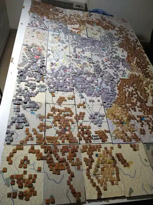 A large, multi-panel hexagonal wargame map is covered with thousands of small, square game pieces representing military…