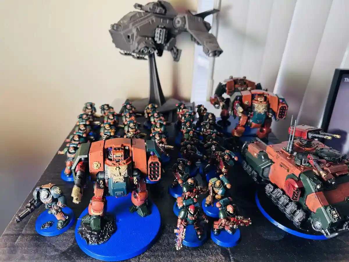 A collection of painted miniature warhammer 40k models, including infantry, tanks, and a large walker mech, arranged on a…