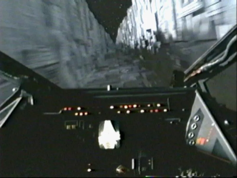 A grainy, first-person view from inside a cockpit, looking forward at a narrow, rocky canyon or tunnel with motion blur…