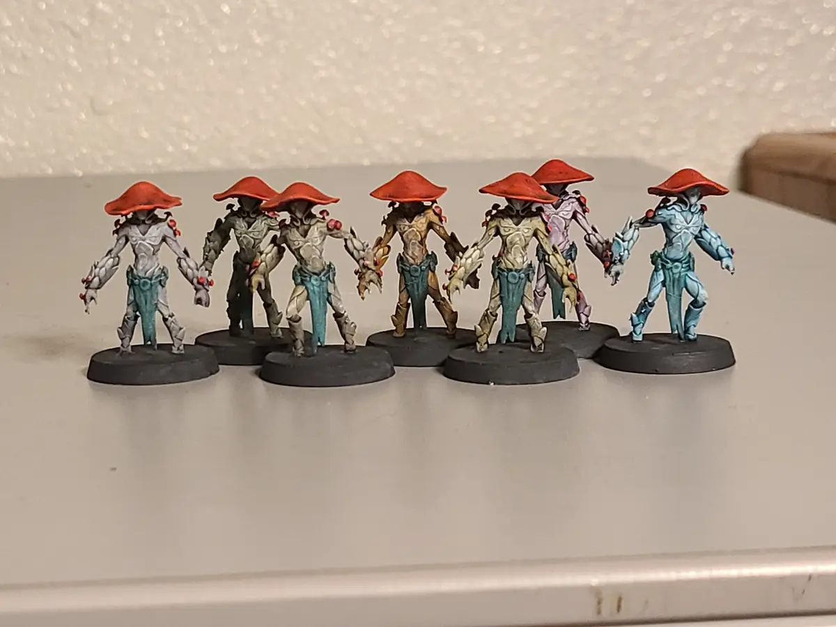 Seven hand-painted fantasy miniatures, each with a red conical hat and distinct color schemes, are arranged in a line…