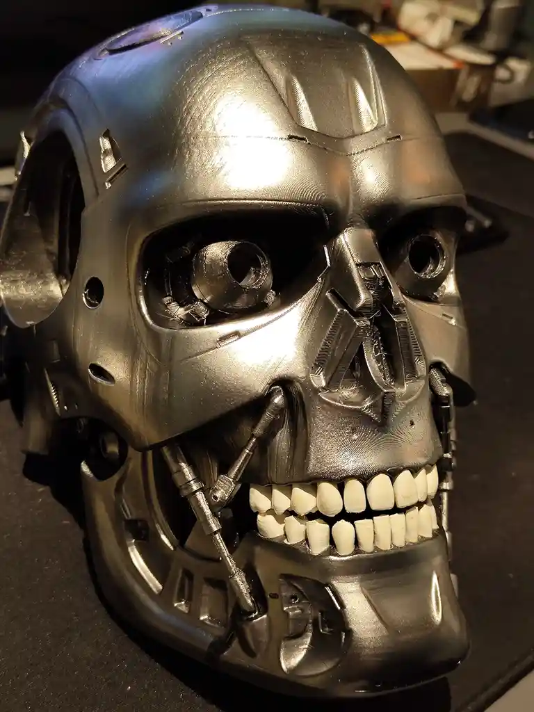 A close-up photo shows a 3d-printed replica of the Terminator's head, featuring a metallic skull with visible layer lines…