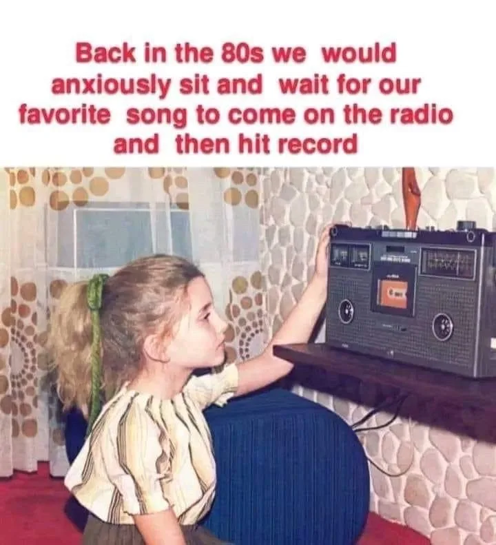 A young girl with blonde hair in a ponytail sits on a blue beanbag chair, reaching up to press the record button on a…