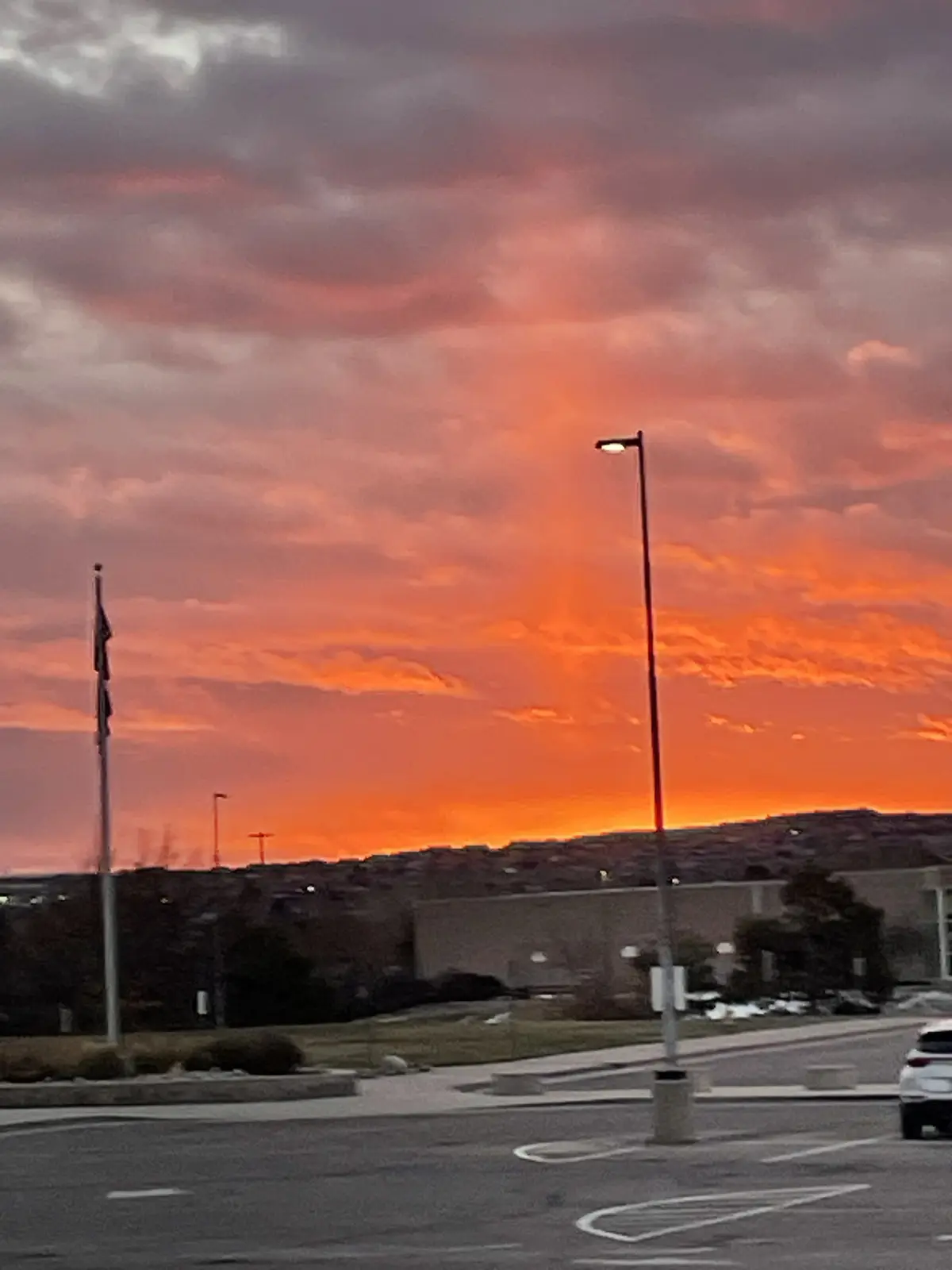 A photograph of a dramatic sunset with fiery orange and pink clouds over a suburban landscape, featuring a streetlamp and…
