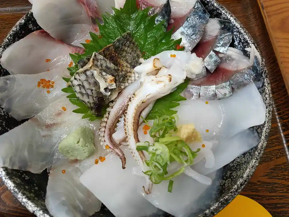 A close-up photo shows a traditional Japanese sashimi platter with assorted raw fish slices, squid, and garnishes like…